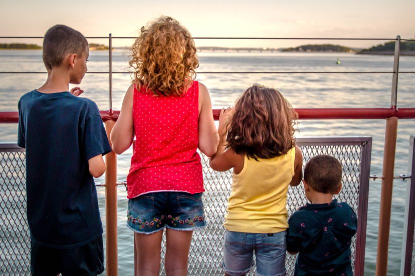 4 children standing and holding a railing facing a body of water.