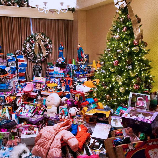 Photograph of room filled with toys, Christmas Tree with lights, and wreath at back.