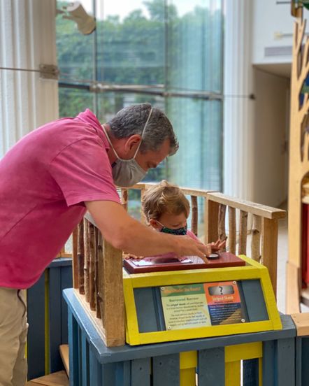 A masked man and child interact with the museums kiosk